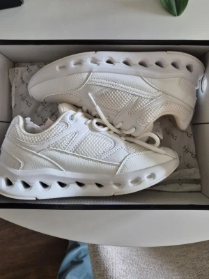 Vita chunky sneakers med meshdetaljer - Säljer ett par vita chunky sneakers med coola håldetaljer i sulan och meshpaneler för extra ventilation. Skorna har en modern och sportig look med snörning och blandning av syntetläder och meshmaterial. Perfekta för dig som gillar trendiga och bekväma skor.Mycket sköna och mjuka!