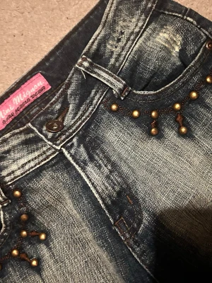 Mörkblå jeans med nitar - Säljer ett par mörkblå jeans från Mini Mignom med slitningar och coola guldfärgade nitar vid fickorna. Har även väldigt coola fickor. De är low waist och klassas som flared eller bootcut. Mått syns på bilder