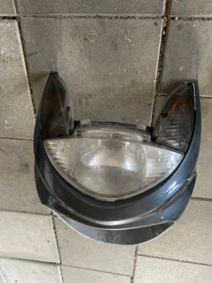 Framlampa till scooter eller moped - Säljer en framlampa till scooter eller moped i svart och genomskinlig plast. Lampan har en bred, rundad form med integrerade blinkers på sidorna. Perfekt om du behöver byta ut din trasiga lampa.
