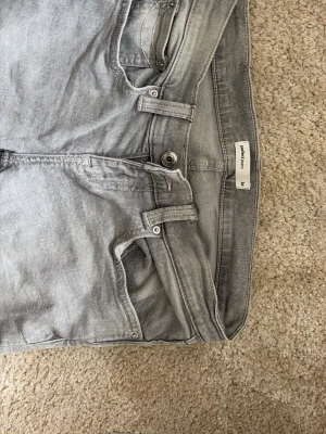 Ljusgrå jeans från Project Raw - Säljer ett par ljusgrå jeans från gina tricot med klassisk femficksdesign och snygga detaljer på bakfickorna. Materialet är mjukt och bekvämt, passar till många olika stilar.