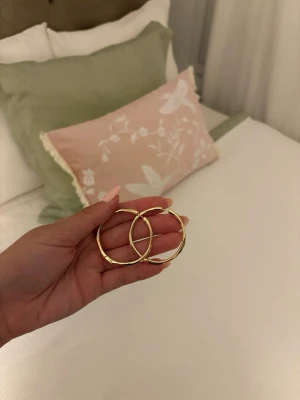 Stora guldiga hoops örhängen - Säljer ett par stora, runda hoops i guldfärgad metall. Örhängena har en enkel och stilren design med en lätt vågig form som ger dem en unik touch. Perfekta för dig som gillar klassiska men ändå trendiga accessoarer.