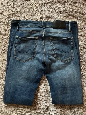 Mörkblå slim fit jeans - Säljer ett par mörkblå slim fit jeans med snygga slitningar och klassiska bakfickor med broderad detalj. Jeansen har normal midja och raka ben. Materialet är mjukt denim som sitter skönt hela dagen.