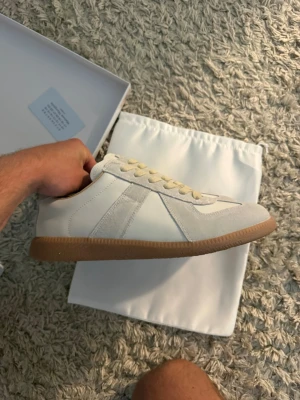 Maison GATS - Stilrena vita sneakers med beige mockadetaljer och klassisk gummisula. Skon har vita och ljusgula snören samt en låg silhuett som passar till många olika outfits. Materialmix av läder och mocka ger en exklusiv känsla.