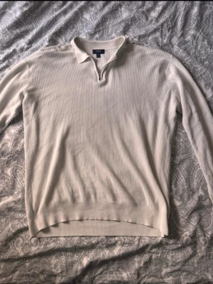 Beige ribbad tröja med krage från SMOG - Säljer en stilren beige långärmad tröja från SMOG i regular fit. Tröjan har ribbad struktur, klassisk krage och dragkedja vid halsen. Perfekt för en clean och avslappnad look. Passar dig som gillar enkel och snygg stil.
