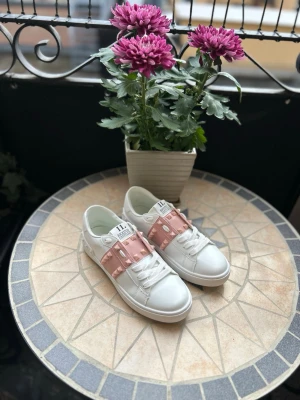 Valentino Garavani Rockstud Skor - Säljer ett par superfina, Valentino Garavani "Rockstud Untitled" sneakers i vitt läder med det klassiska rosa bandet och nitar över vristen. Tyvärr passade de inte min tjej så de säljes vidare. 
