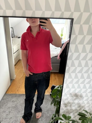 Rosa pikétröja från Fred Perry - Säljer en klassisk rosa pikétröja från Fred Perry med vit broderad logga på bröstet. Tröjan har korta ärmar, krage och knappar vid halsen. Perfekt för dig som vill ha en stilren och sportig look.