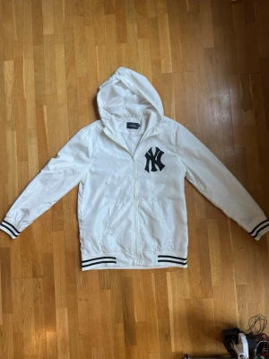 New era jacka - Snygg vit hoodie med svart NY-logga på bröstet. Jackan har dragkedja framtill, två fickor och huva.  Passar perfekt personer som är ca 185 cm långa. Efter som new era är extremt små i storleken