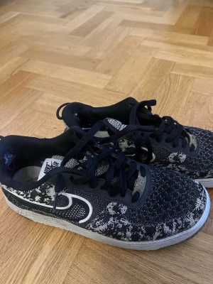 Nike Air Force 1 svarta mönstrade sneakers - Svarta Nike Air Force 1 sneakers med vitt mönster och vit sula. Skorna har klassisk låg profil, svarta skosnören och tydlig Nike-logga på sidan. Ovandelen är i textil med unikt mönster och detaljer i vitt och grått. Finns litet hål inne, se bild, därav pris 