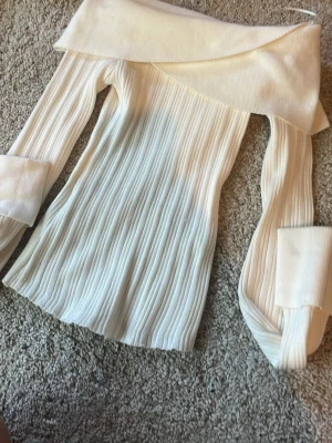 Offshoulder ribbad topp från Bershka - Superfin offshoulder topp från Bershka i ribbat material. Toppen är krämvit, har långa ärmar med breda muddar och en snygg omlottkrage. Perfekt för dig som vill ha en trendig och stilren look.