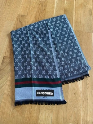 Grå halsduk - INSTABOX!!! Snygg grå halsduk. Halsduken har en bred rand i grönt och rött samt svarta fransar i kanterna. Materialet ser ut att vara mjukt och följsamt, perfekt för att lyfta din outfit. Skriv efter tydligare bilder. 
