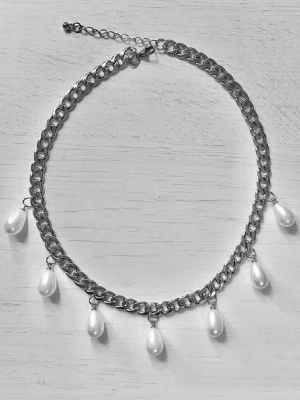 Kedjehalsband med droppformade pärlor - Snyggt halsband med grov silverfärgad kedja och fem droppformade vita pärlor som hänger längs kedjan. Justerbar längd med förlängningskedja. Perfekt för att ge en cool touch till din outfit.