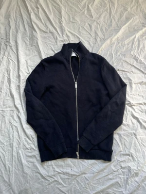 Svart stickad ziptröja SELECTED - Svart stickad ziptröja från SELECTED med hög krage och hel dragkedja framtill. Tröjan har ribbade muddar vid ärmslut och nederkant, perfekt för lager-på-lager och en clean look.
