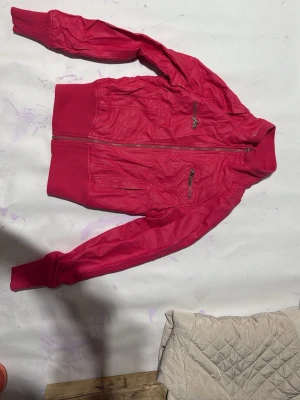 Rosa bomberjacka från Fishbone - Snygg rosa bomberjacka från Fishbone med glansigt foder och ribbade muddar. Jackan har dragkedja framtill, två bröstfickor med dragkedja och en klassisk bomberjacke-look. Perfekt för dig som vill sticka ut med färg.