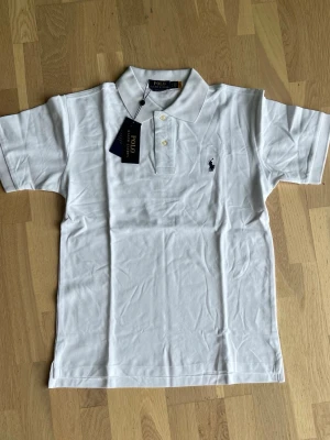 Ralph Lauren White polo shirt size M - Brand new, never worn Polo Ralph Lauren Custom Slim Fit polo shirt in White. Comes with original tags attached and original packaging.  * Condition: Brand New with Tags (NWT) * Color: White * Fit: Custom Slim Fit * Size: M * Material: 100% Cotton * No flaws, stains, holes, or signs of wear. * Authentic Polo Ralph Lauren. * Retail ≈ 180$ A timeless wardrobe essential, perfect for both casual and smart-casual outfits. 