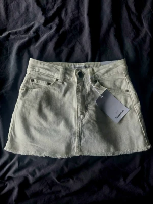 Vit jeanskjol från Pull&Bear - Trendig vit jeanskjol från Pull&Bear med rå kant nertill och klassisk femficksdesign. Kjolen har även inbyggda shorts, bälteshällor och knappstängning framtill. Perfekt för dig som gillar en enkel men snygg stil. Kjolen är helt ny och aldrig använd pågrund av fel storlek, så lappen mm är fortfarande kvar.