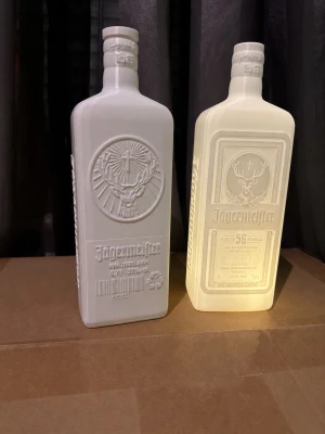 Jägermeister flaska formad lykta - Unik lampa i form av en Jägermeister-flaska, tillverkad i vit plast med detaljerat reliefmönster och text. Lampan ger ett mjukt sken och är perfekt som dekoration i hemmet eller till baren. Säljs med led värme ljus