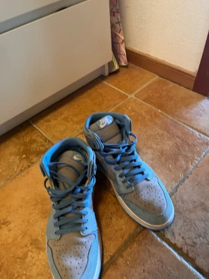 Blå och grå Nike Air Jordan sneakers - Snygga Nike Air Jordan sneakers i blått och grått med högt skaft. Skorna har klassisk swoosh på sidan, perforerad tå och vita detaljer. Materialet är en mix av mocka och textil vilket ger en schysst streetlook.