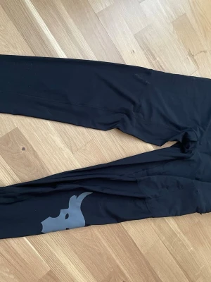 Svarta träningsleggings underarmour  - Säljer ett par svarta tränings leggings för herr med grå logga på benet från Underrmour De har en tight passform och är tillverkade i ett stretchigt material som passar perfekt till träning eller chill. Snygg och enkel design med diskret detalj på benet.
