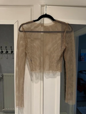 Glittrig mesh topp med lång ärm - Glittrig mesh topp i beige med lång ärm. Toppen är genomskinlig och har ett nätmönster med små glittrande detaljer som fångar ljuset. Storlek XS. Aldrig använd