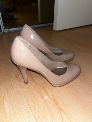 Beige lackade pumps med medelhög klack - Säljer ett par stilrena pumps i beige lackat material med rundad tå och medelhög smal klack. Klassisk modell som passar till många olika outfits.