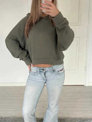 Scuffers liknande hoodie - Säljer en olivgrön cropped hoodie med huva och långa ärmar. Hoodien har en avslappnad passform och breda muddar vid ärmslut och nederkant. Perfekt för en chill och trendig look. Materialet känns mjukt och bekvämt mot huden.