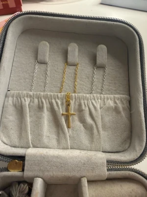 Guldigt halsband med korshänge - Snyggt halsband i guldfärgad metall med ett enkelt korshänge. Kedjan är tunn och stilren, vilket gör att korset verkligen står ut. Perfekt för dig som gillar minimalistiska smycken med en klassisk touch. Passar till många olika stilar och är lätt att matcha med andra accessoarer. Halsbandet är egengjort i rostfritt stål.