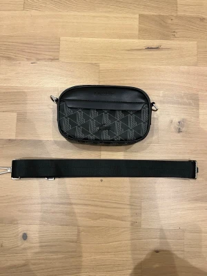LACOSTE AXELVÄSKA (HERR) - helt ny lacoste axelväska säljs eftersom den inte används längre, oanvänd och inga skador. Väskan är äkta och är köpt i lacoste butiken i frankrike men inget kvitto tillkommer och bandet är justerbart  