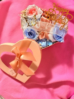 Hjärtformad presentbox med rosor - Handgjorda satinblommor i en perfekt presentbox. Inuti finns konstgjorda rosor i blått, rosa och vitt, dekorerade med en guldfärgad 'Happy Birthday'-skylt och en liten fjäril som ingår. Går även att ta bort happy birthday/sätta fast den om det önskas 😊 perfekt för present eller dekoration till hemmet 