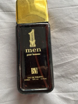 1 Men pour homme Eau de Toilette - En maskulin parfymflaska med mörkbrun glasdesign och guldfärgat lock. Flaskan rymmer 100 ml och har elegant guldtext på framsidan. Doften är en Eau de Toilette och passar dig som vill ha en klassisk och stilren parfym i badrumshyllan. Halva parfymen kvar