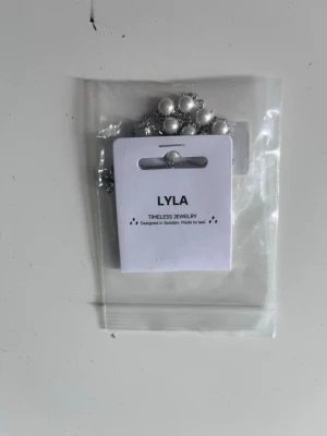Silverhalsband med vita pärlor från LYLA - Snyggt halsband från LYLA med silverfärgad kedja och vita pärlor jämnt utspridda längs hela halsbandet. Aldrig använt. 