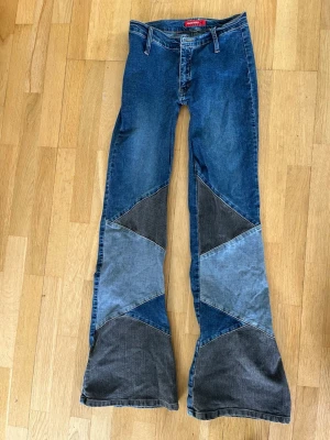 Miss sixty utsvängda jeans patchwork  - Unika patchwork jeans med utsvängda ben i olika blå och grå nyanser. Jeansen har hög midja och coola kontrastsömmar. Materialet är denim och de har en riktigt retro 70-talsvibe. Perfekta för dig som vill sticka ut med din stil! Storlek: 29/32, men små i midjan. Obs! Du måste sy i en knapp då den saknas 