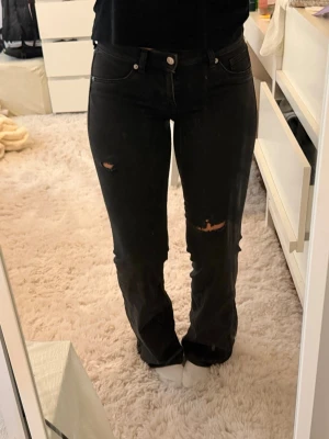 Svarta slitna bootcut jeans - Säljer ett par svarta bootcut jeans med slitningar på låren och knäna. Jeansen har klassisk femficksmodell, normal midja och är tillverkade i denim med lite stretch för skön passform. Perfekta för en avslappnad och trendig look.
