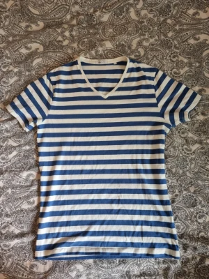 Randig Kvalitéts t-shirt - Säljer en klassisk t-shirt från Bläck med blå och vita horisontella ränder. Tillverkad i mjuk bomull som känns skön mot huden. Har tyvärr en liten fläck mitt på tröjan men inget som inte går bort i tvätten. Perfekt för dig som gillar en enkel men stilren look.