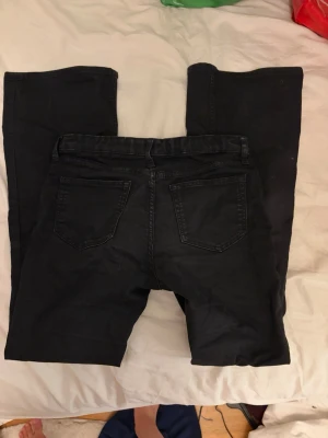 Svarta flare jeans från H&M - Säljer ett par svarta flare jeans från H&M med låg midja och justerbar midja. Jeansen har klassiska bakfickor och är tillverkade i ett mjukt denimtyg. Perfekta för dig som gillar en retro och trendig look.