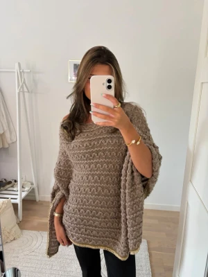 Beige stickad poncho - Säljer en beige stickad poncho med vågigt mönster och guldfärgad kant. Står varken vart den är ifrån eller vilken storlek de är, men skulle gissa på en M❤️