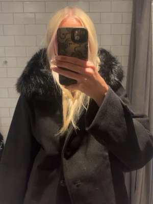 Svart kappa med fuskpäls - Säljer en svart kappa med stor, fluffig fuskpäls runt huvan. Kappan har knäppning framtill, Från ginayoung köpt förra hösten strl Xs, toppen skick!!