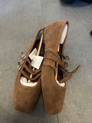 Bruna ballerinas med spännen - Snygga ballerinas i brun mocka från M&S med fyrkantig tå och tre tunna remmar med silverfärgade spännen. Skorna har en stilren och trendig look som passar perfekt till jeans eller kjol. Superfina detaljer och mjukt material. Helt Ny!