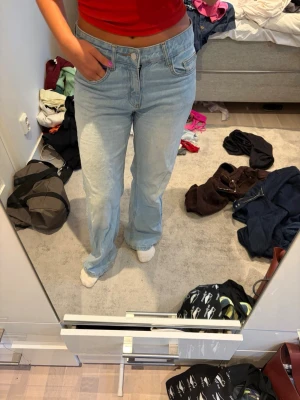 Ljusblå raka jeans med hög midja - Säljer ett par ljusblå jeans med rak passform och hög midja. Jeansen har klassiska fem fickor och stängs med knapp och dragkedja. Tillverkade i denim med en avslappnad vibe, perfekta till en casual look. Lite slitna nertill