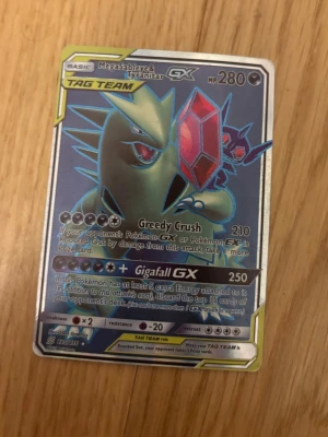 Pokémonkort Megasableye & Tyranitar GX - Säljer ett Pokémonkort med Megasableye & Tyranitar GX TAG TEAM. Kortet har en holografisk yta och coola illustrationer i grönt, rött och blått. Perfekt för samlare eller dig som vill boosta din lek med kraftfulla attacker som Greedy Crush och Gigafall GX. Väldigt rare