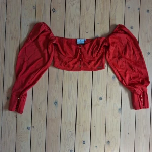 Röd croppad topp från ODolls - Trendig röd croppad topp från ODolls med offshoulder-design och långa puffärmar. Toppen har knappar framtill och en snygg, figurnära passform. 