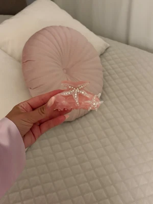 Rosa hårklämma med sjöstjärnor - Superfin hårklämma i ljusrosa akryl med dekorativa sjöstjärnor prydda med glittrande stenar och pärlor. Perfekt accessoar för att ge en söt och trendig touch till din frisyr.