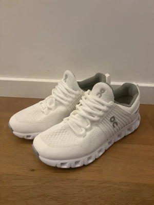 Vita sneakers från On - Snygga helvita sneakers från On med sportig design och ventilerande meshmaterial. Skorna har en chunky sula och diskreta logodetaljer på sidan och plösen. Perfekta för dig som gillar stilrena och bekväma sneakers.