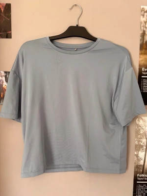 Ljusblå basic t-shirt - En enkel ljusblå t-shirt med rund hals och korta ärmar. T-shirten har en loose passform och är gjord i mjuk bomull, perfekt för en avslappnad stil. Passar till det mesta och är lätt att matcha med andra plagg. Obs en liten fläck av foundation som inte syns vid användning. 