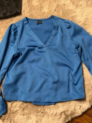 Blå v-ringad blus med puffärm - Snygg blå blus med v-ringning och långa puffärmar. Tillverkad i ett lätt, strukturerat tyg som ger en trendig look. Perfekt att styla med jeans eller kjol för en cool vardagsoutfit.