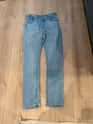 Ljusblå raka jeans från Levi's - Snygga ljusblå jeans från Levi's med klassisk femficksdesign och raka ben. Jeansen har en ikonisk läderpatch bak i midjan och röda Levi's-detaljer på bakfickan. Perfekta för en avslappnad och trendig stil.