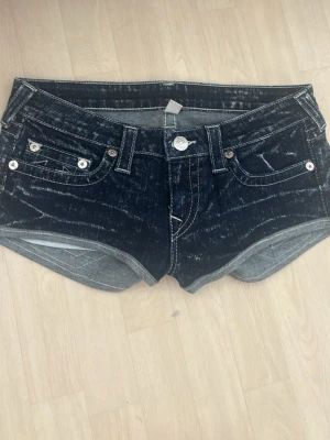 Mörkblå jeansshorts True Religion - Snygga mörkblå jeansshorts från True Religion med slitna detaljer och kontrastsömmar. Klassisk femficksmodell med silverfärgade knappar och logga på bakfickan. 