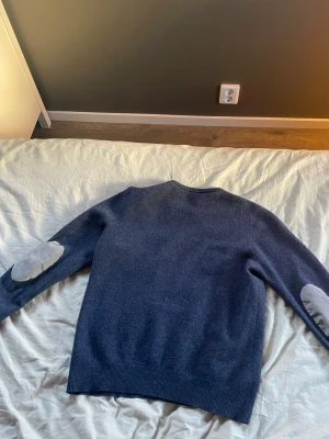 Blå stickad tröja Gran Sasso - Det är en storlek s som har krympt så cashmerem känns lite tjockare och lite lite annorlunda Mysig blå stickad tröja från Gran Sasso i cashmere och ull. Tröjan har rund halsringning, ribbade muddar och ljusgrå armbågslappar som snygg detalj. Perfekt för dig som gillar klassisk men ändå trendig stil.