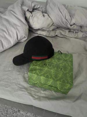 Svart keps med grön-röd rand - Snygg svart keps med diskret mönster och en grön-röd rand på sidan. Klassisk böjd skärm och sex paneler. Passar perfekt till streetwear och har en stilren look.