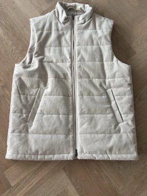 John Henric Väst  - Säljer en splitterny John Henric Väst i manchester material. En vit/beige väst i storlek L som aldrig är använd. En väldigt skön väst som passar väldigt bra till hösten med ett skönt innermaterial. Säljs inte längre och är väldigt true to size så har man L så sitter den bra. Har man M så kan den också fungera.