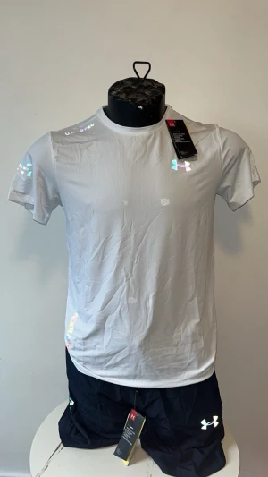 Vit t-shirt från Under Armour - Snygg vit t-shirt från Under Armour med rund hals och korta ärmar. Tillverkad i ett lätt och funktionellt material som passar perfekt till träning. Diskret logga på bröstet och ärmen. Enkel och sportig design.